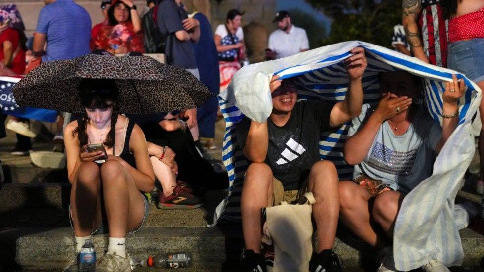 People take cover from the rain amid stormy weather ahead of a Fourth of July rally featuring U.S. President Donald Trump to mark the 250th anniversary of U.S. independence, in Washington, D.C., U.S., July 4, 2026.