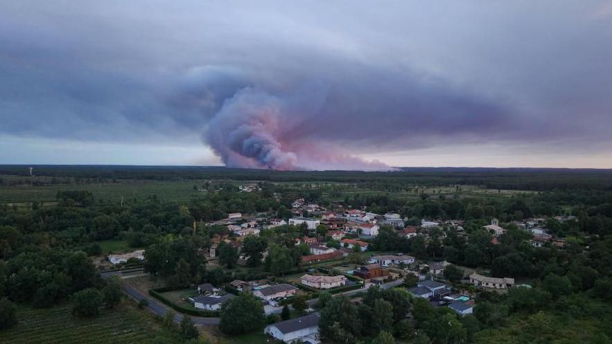 A done view showing the Sainte-Helene commune in France with smoke rising in the background during a wildfire in a forest area in Saumos