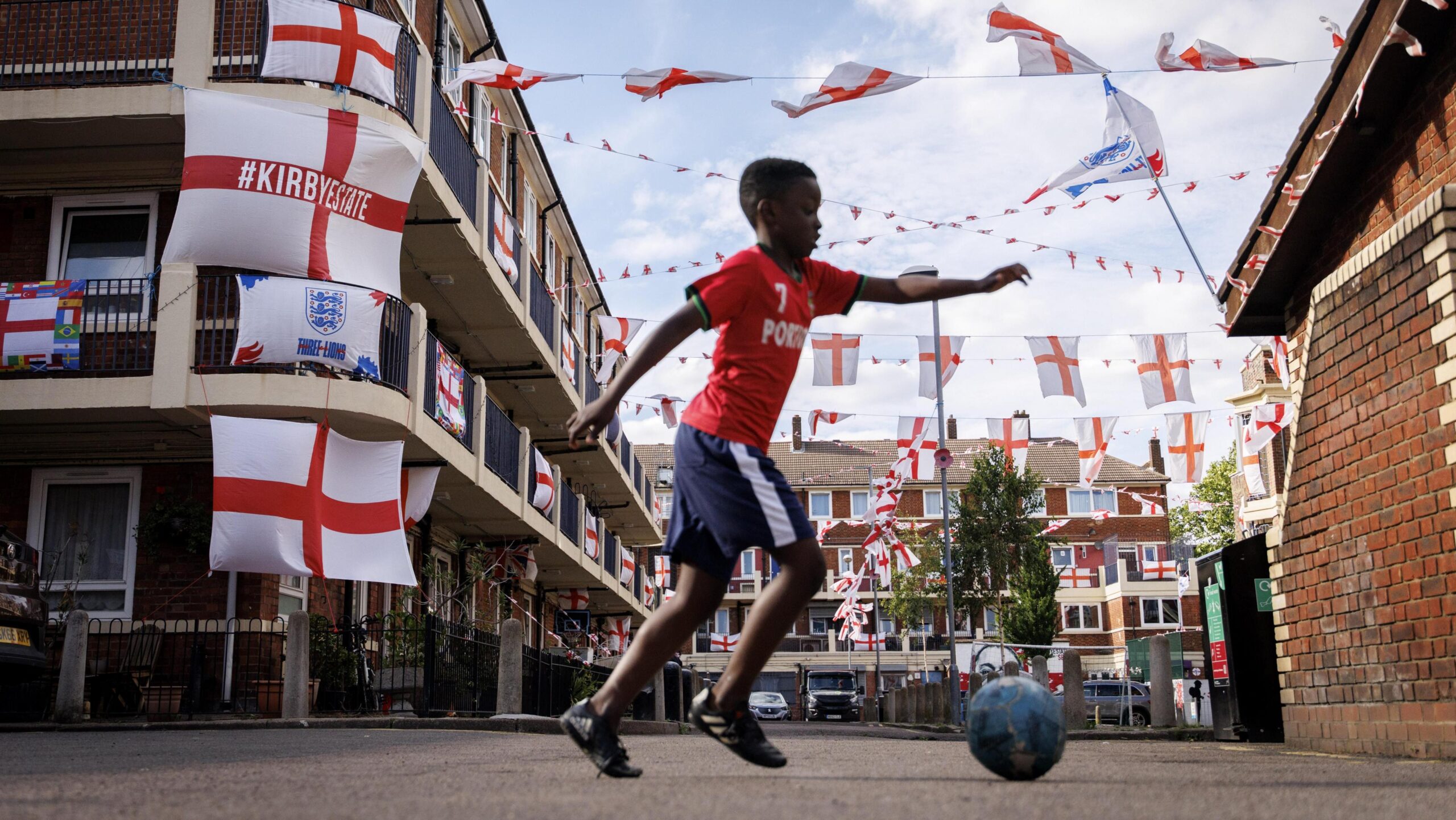 A boy plays football in a housing estate in London decorated with England flags.