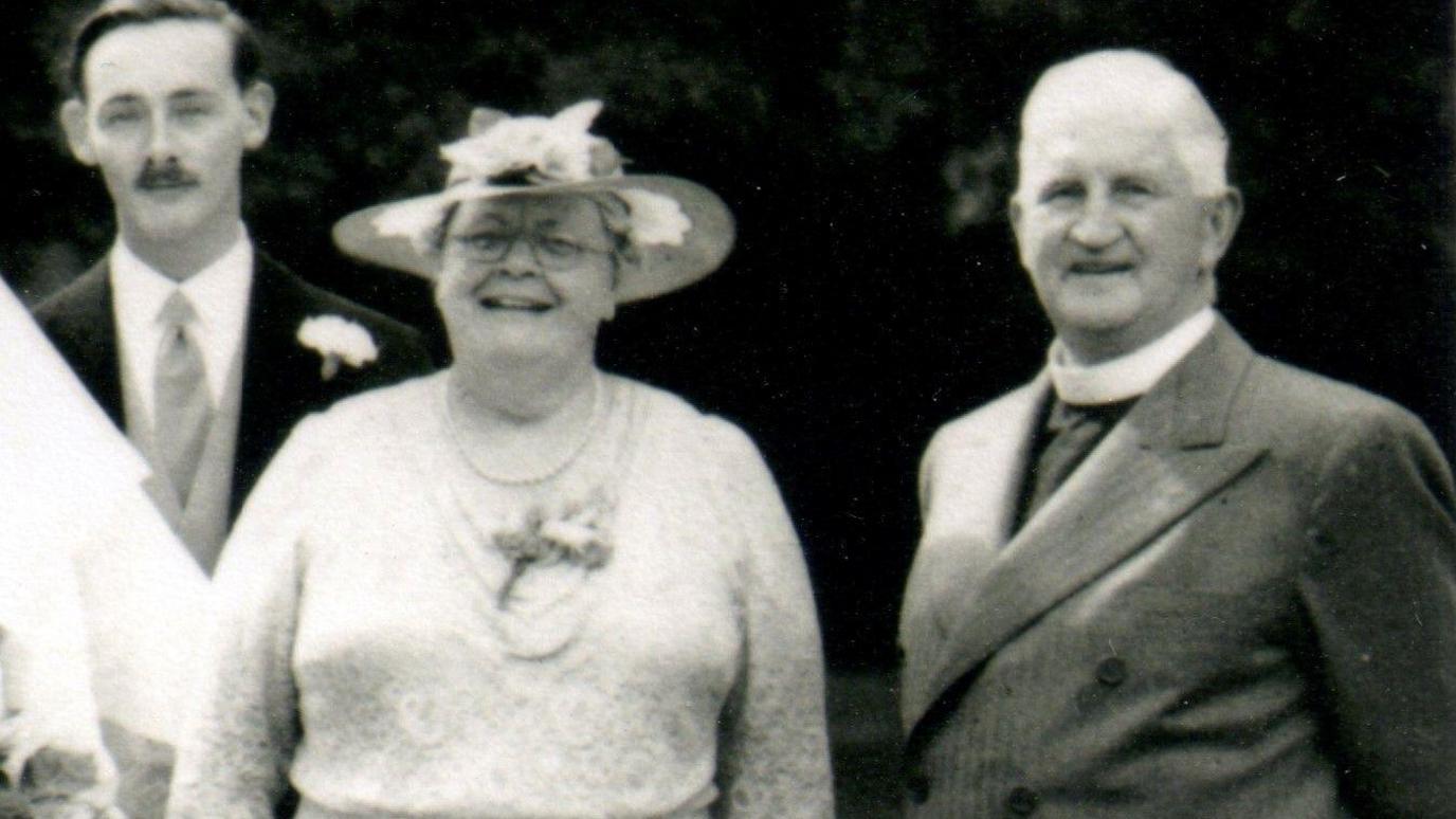 A black and white image of Eileen Elgar with Alfred, her husband, and another man behind them. She is wearing a hat.