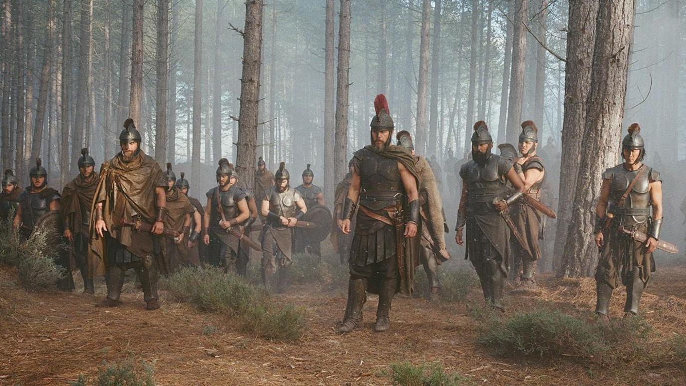 Matt Damon, centre, as Odysseus, stands with a group of men in Greek armour and helmets in Culbin Forest.