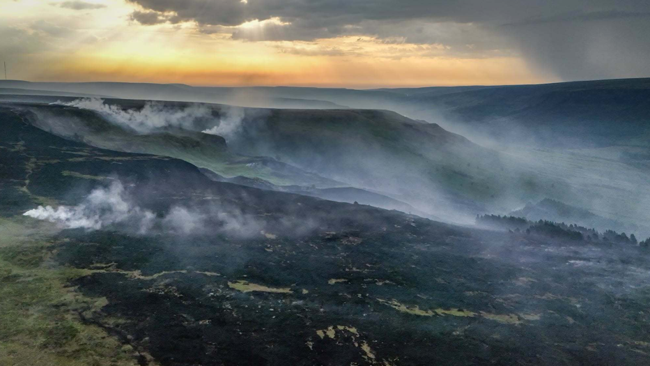 Smoke rises from a large area of scorched ground following a wildfire in Glossop, Derbyshire on June 25