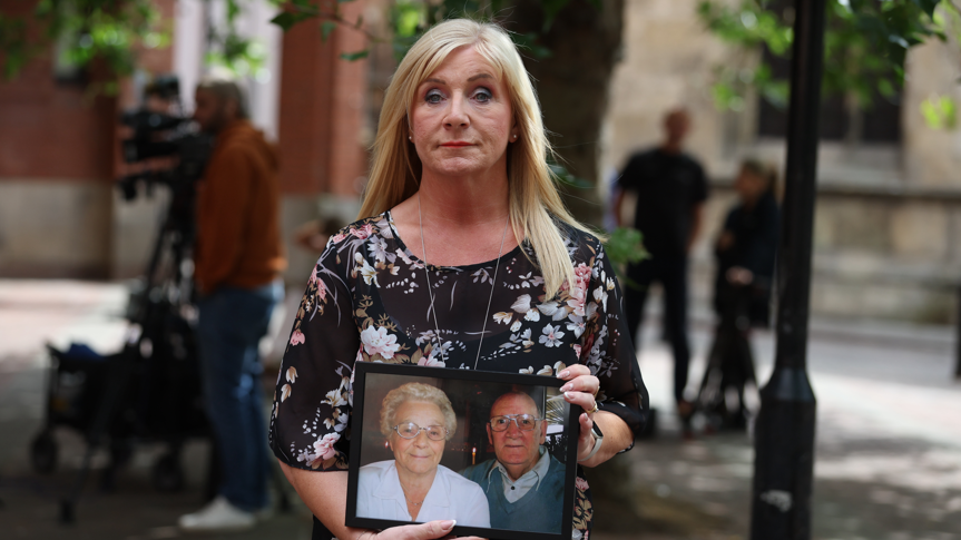 Karen Dry, holding a photo of her parents, outside Hull Crown Court. She has long blonde hair and is wearing a black floral dress.
