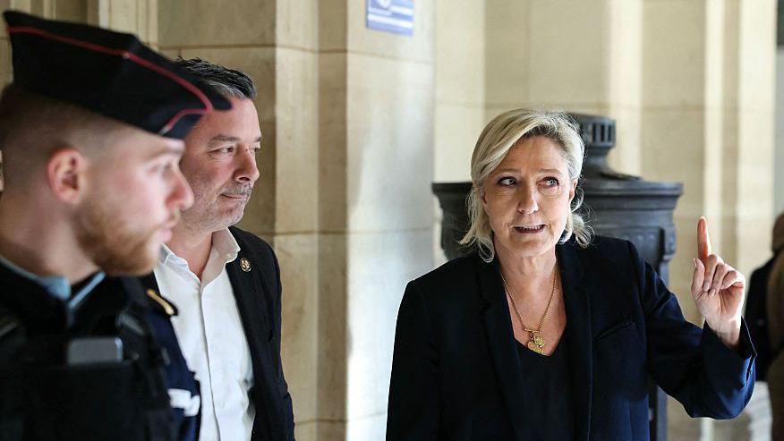 Marine Le Pen gestures as she arrives after a break in the defense's closing argument in the trial of far-right party Rassemblement National (RN) former or actual members on charges of embezzlement of European public funds in a case of alleged European Parliament fake jobs at the Palais de Justice in Paris on February 4, 2026