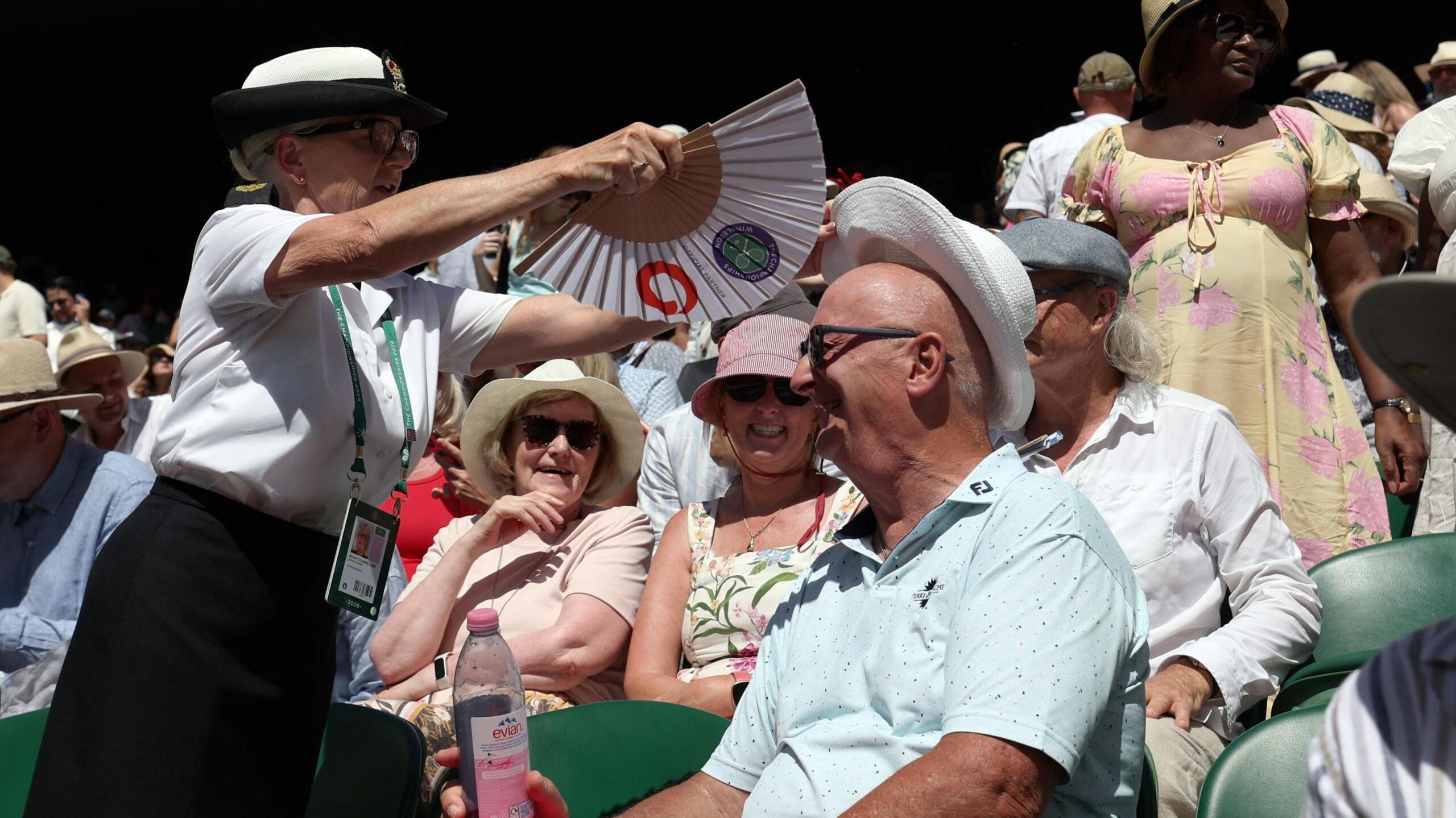 A steward uses a handheld fan to cool down a smiling spectator at Wimbledon.