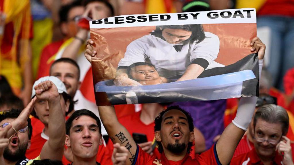 A Spain fan holds up a banner depicting Lionel Messi bathing Lamine Yamal as a child during a Euro 2024 match