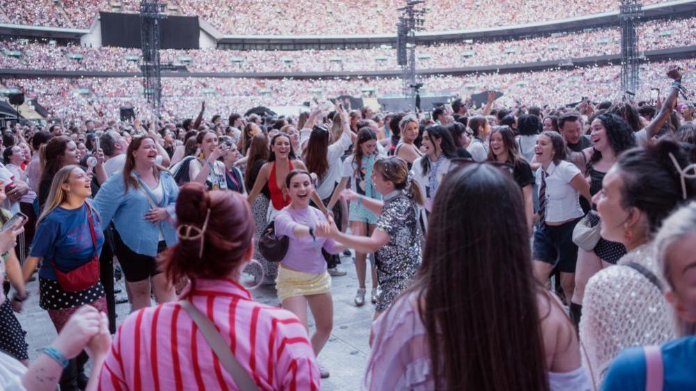 Fans, many female and wearing sparkly skirts and dresses, can be seen dancing in the standing area of Wembley Stadium during Styles' concert on Saturday. Thousands of other people can be seen in the background