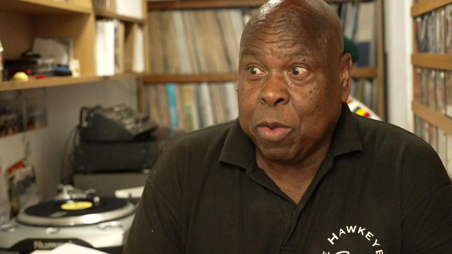 Roy Forbes-Allen in a Hawkeye Records polo shirt sits among shelves of vinyl records and turntables