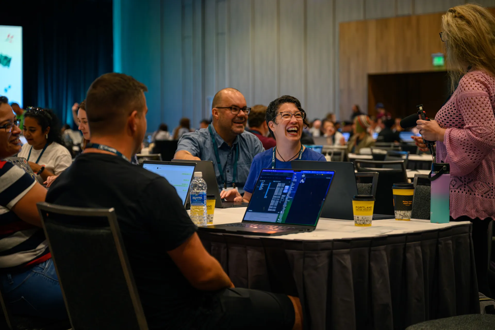 WordCamp attendees laughing together around a table of open laptops.