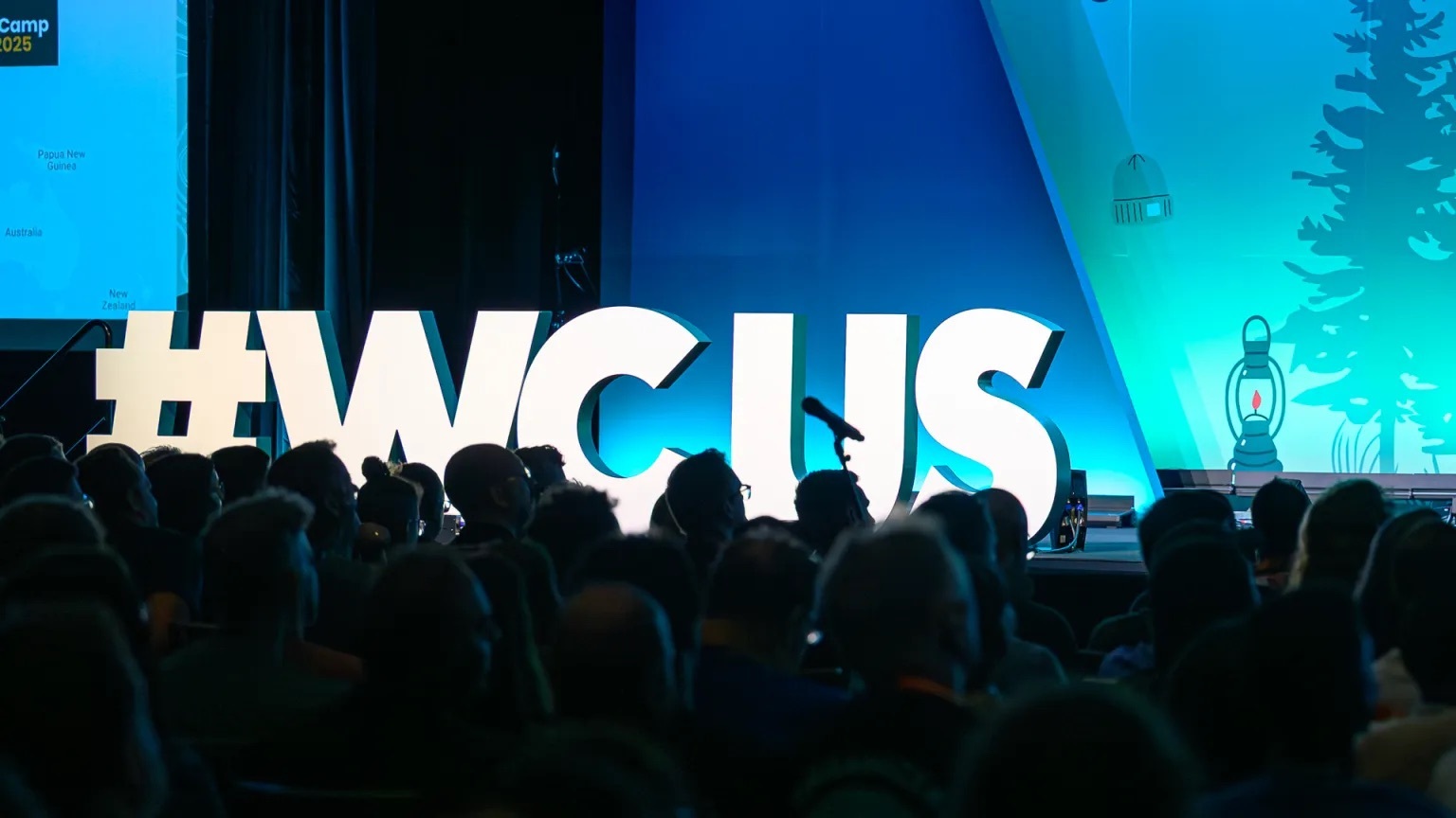 Large illuminated hashtag WCUS letters on stage in front of a silhouetted WordCamp US audience during a session
