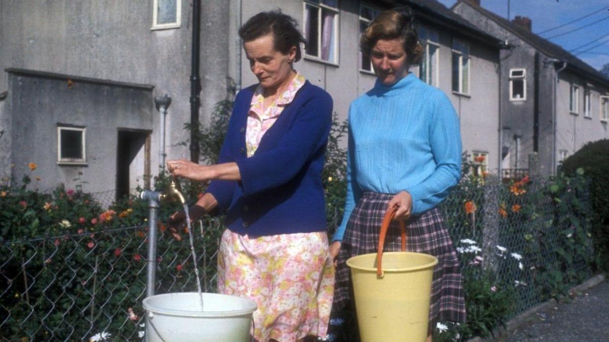 Archive photo of two women filling up buckets with water from a standpipe