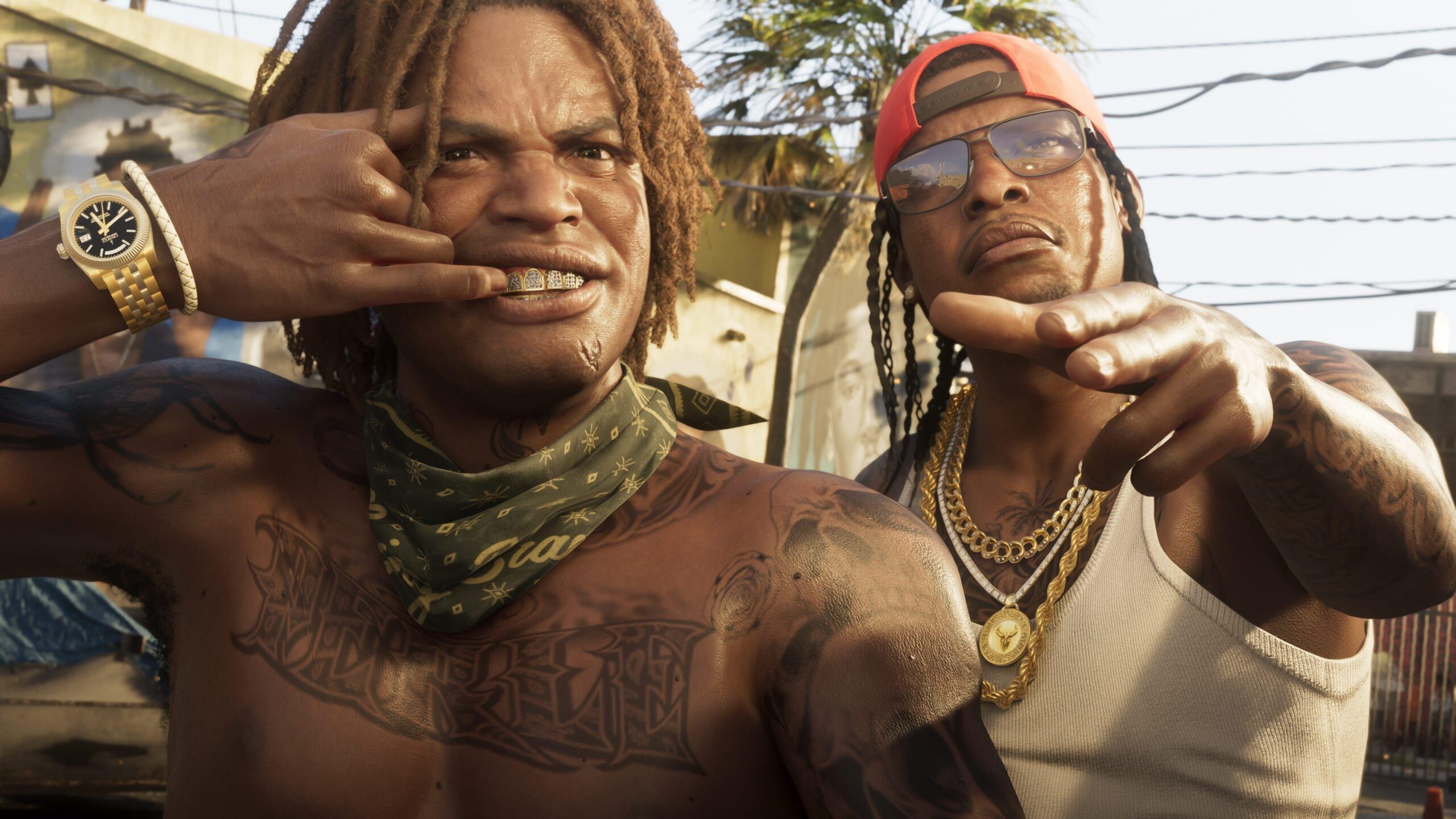 Two characters from GTA 6 gesture at the viewer. One, wearing a heavy gold watch, pulls back his top lip to reveal teeth covered in gold. The man next to him wears three thick, gold chains, one with a large round medallion attached. Both are heavily tattooed. The image is convincingly lifelike despite being computer generated