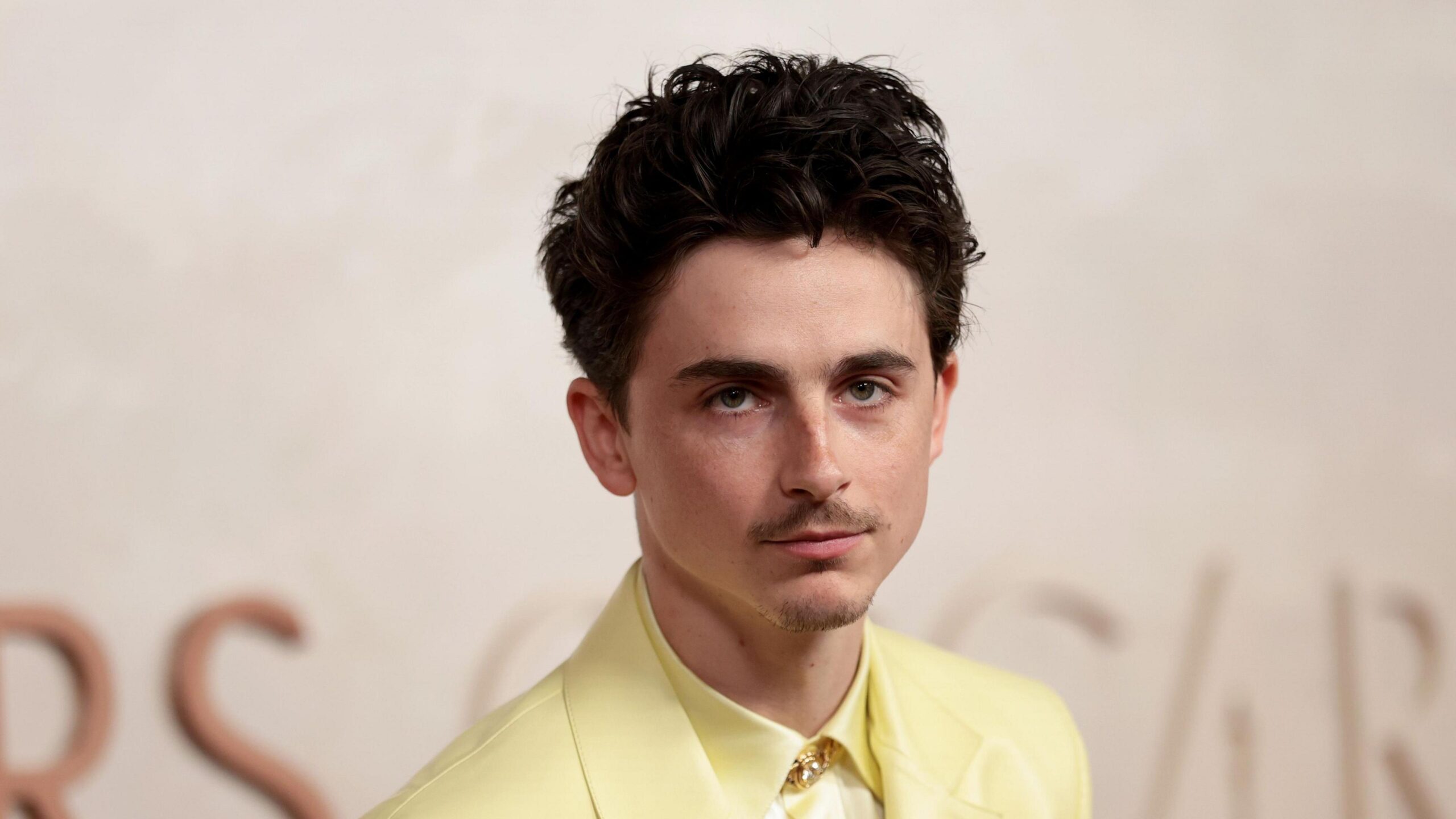 Timothée Chalamet wears a butter yellow suit with a gold pin on the collar.