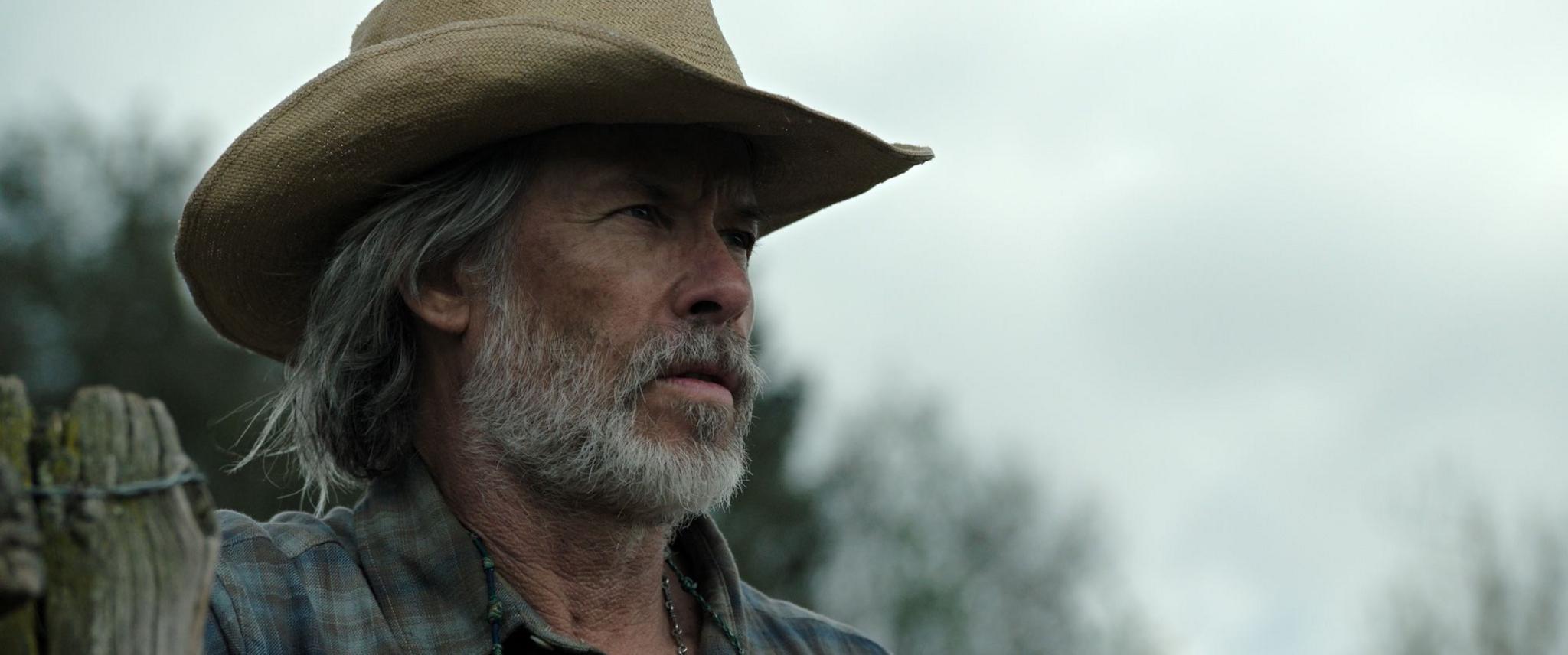 Still from The Dog Stars of Guy Pearce as Pops, wearing a beige cowboy hat and sporting an unkempt beard and hairstyle.