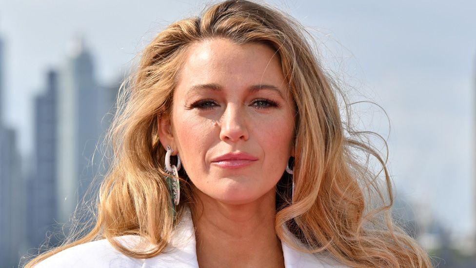 Blake Lively in a white suit and earrings posing in front of the London  skyline on 8 August 2024