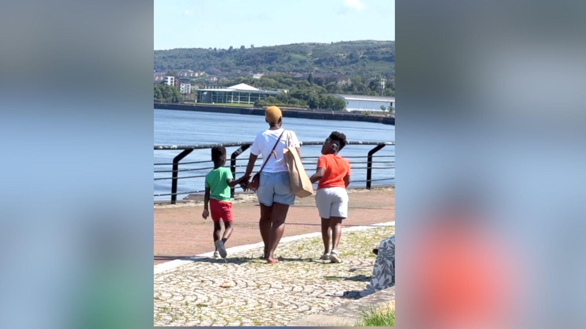A mother walks her two children by the riverside.