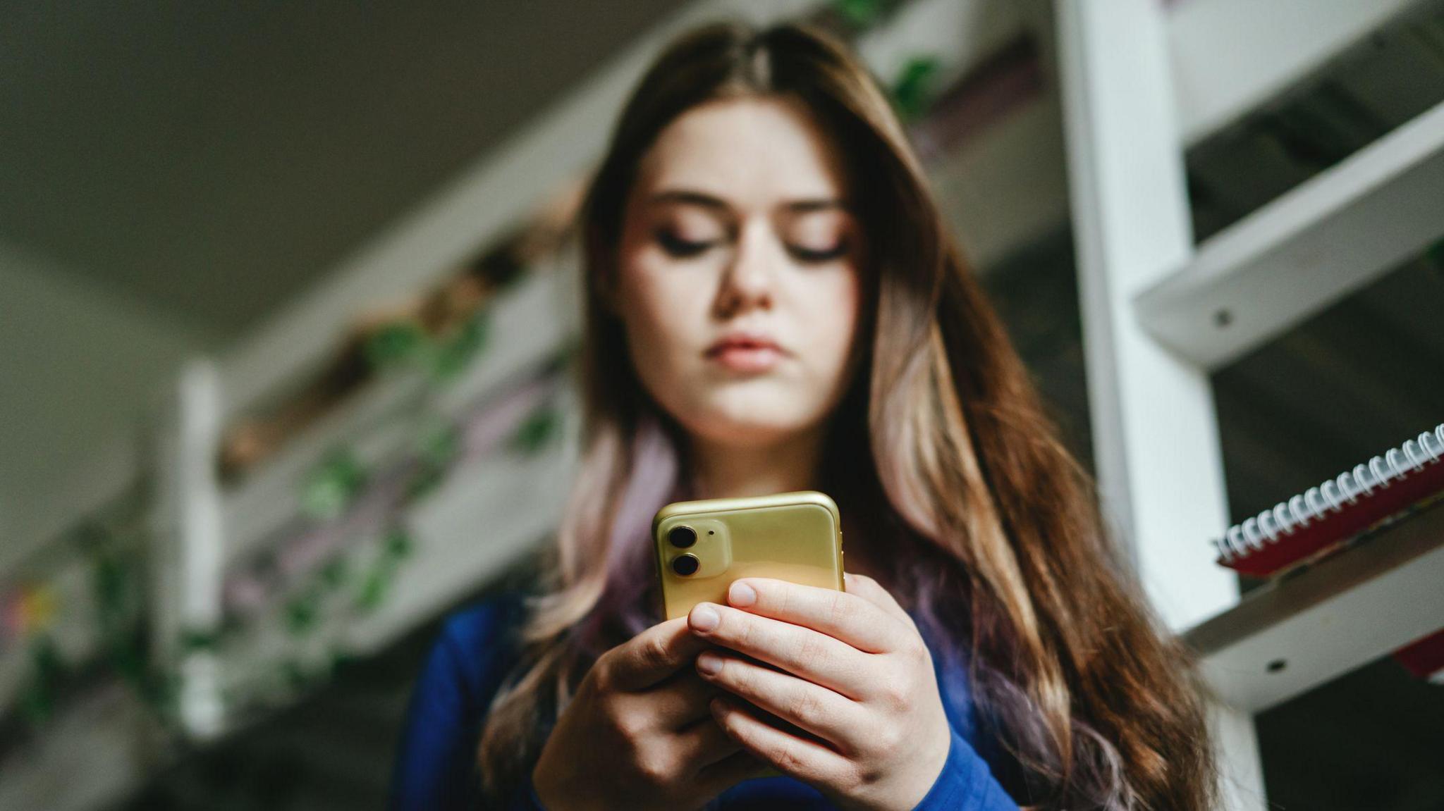 A young woman looks down at her mobile phone.