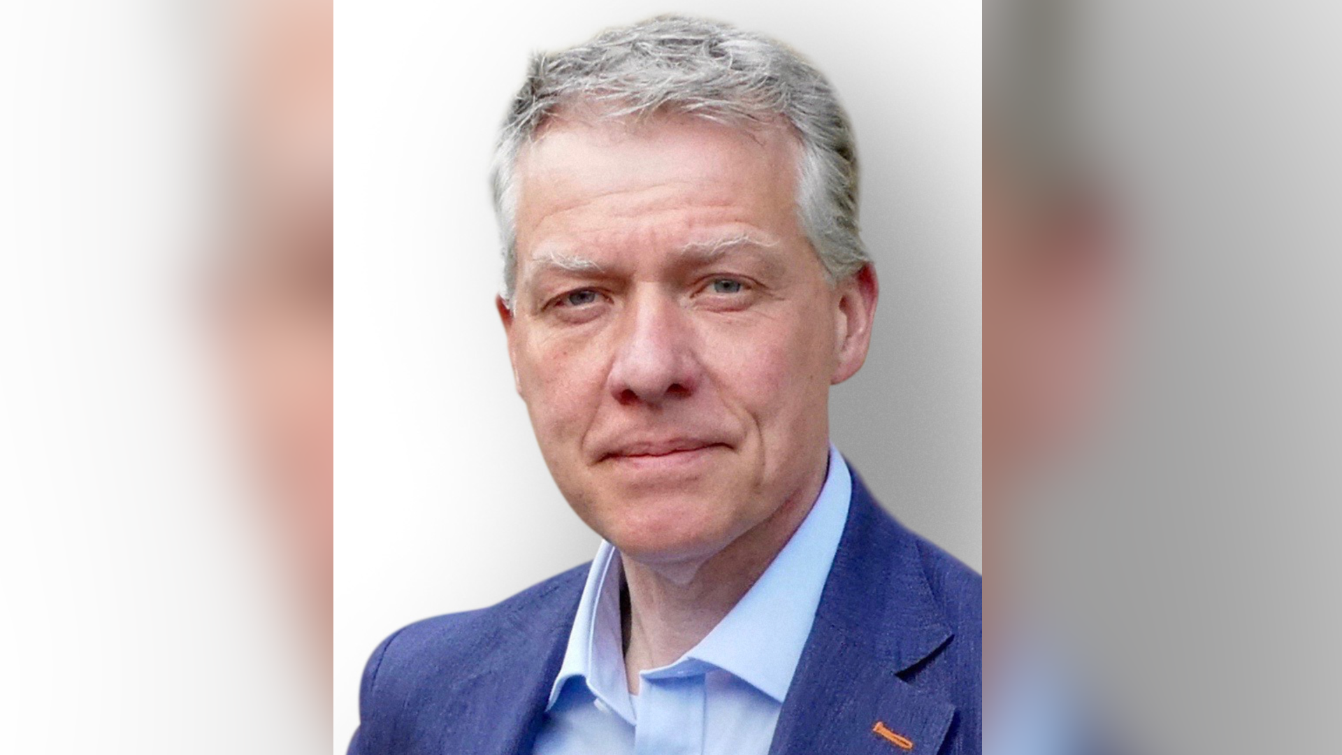 William Clouston who has grey hair wears a dark blue jacket and an open necked light blue shirt.
