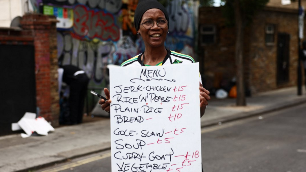 A woman holds a hand-written sign advertising food prices on a menu.