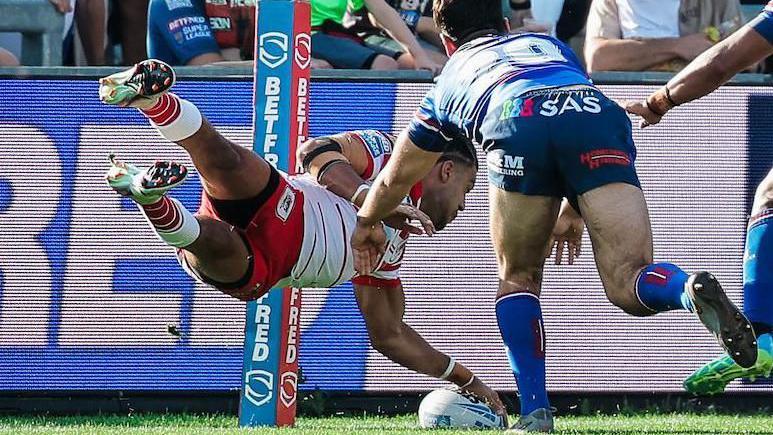St Helens wing Lewis Murphy scoring a try for his side by diving for the line with his left hand on top of the ball which is grounded on the line while two Wakefield defenders try to stop him