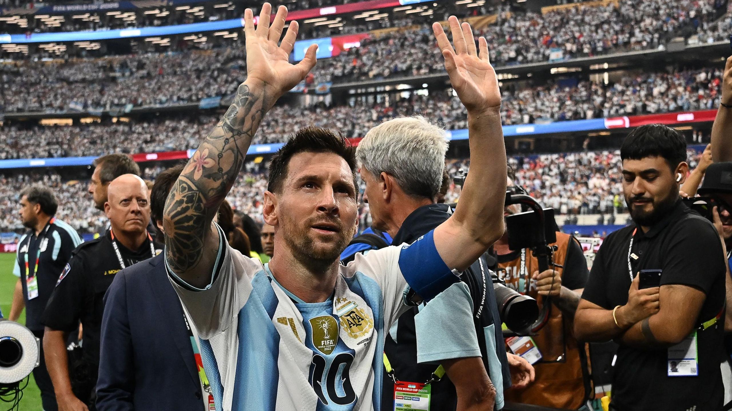 Lionel Messi, wearing Argentina's number 10 shirt, with light blue and white stripes, raises his arms in appreciation