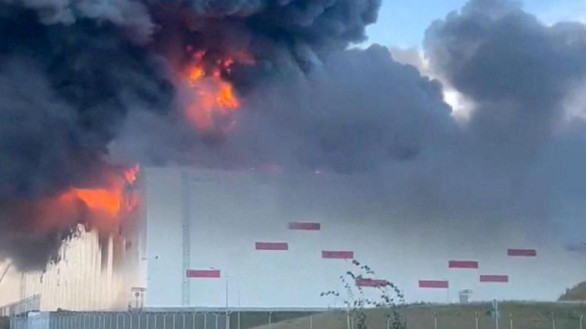 Huge flames and black smoke rise from a warehouse with similar design to other Wildberries warehouses