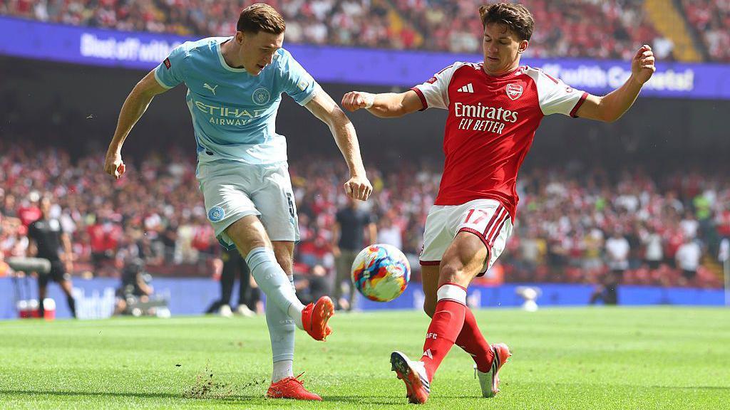 Manchester City's Elliot Anderson and Arsenal's Christos Tzolis battle for the ball, which can be seen just off the floor between both players
