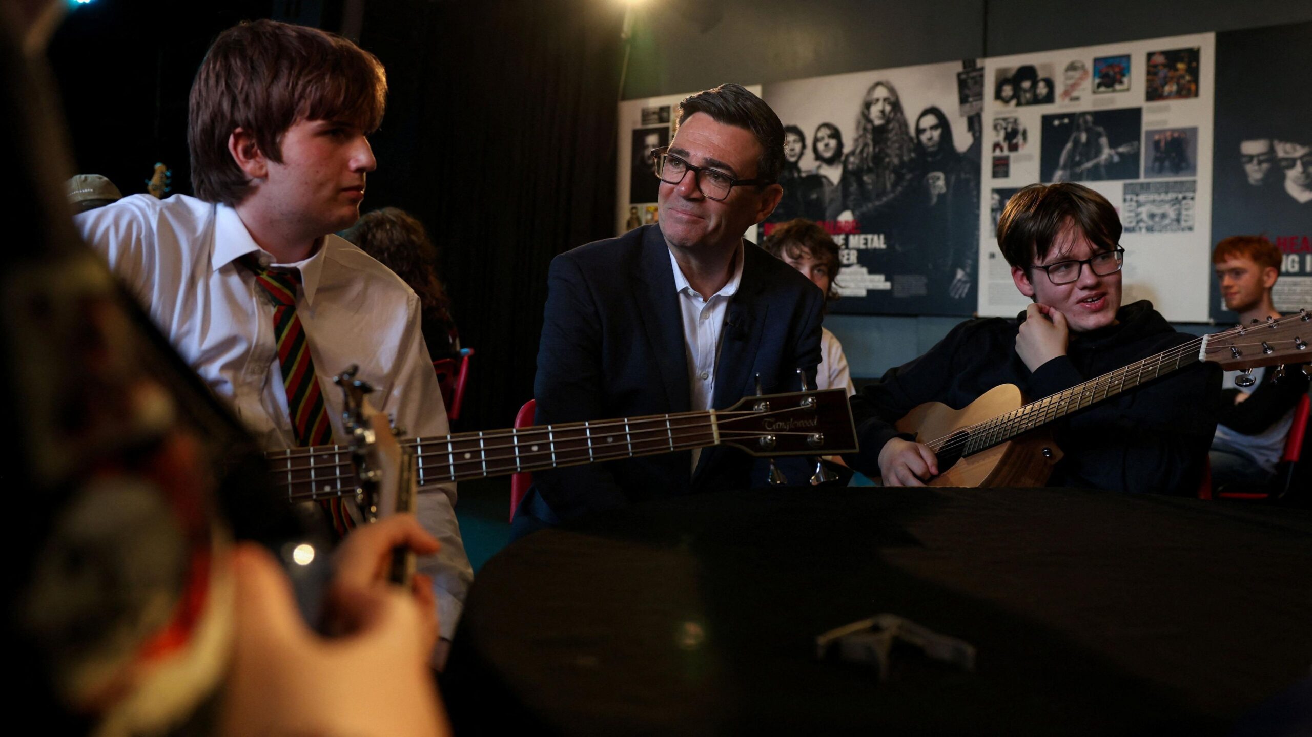 Prime Minister Andy Burnham speaks to young people during a visit to The Oh Yeah centre in Belfast. The young people are playing guitars.
