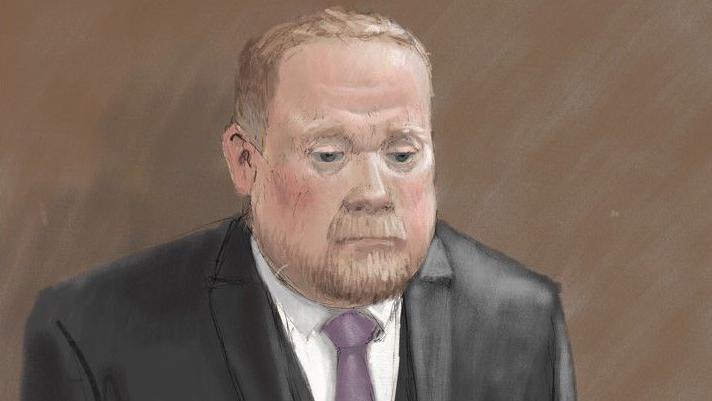 Courtroom sketch of Robert Bush in a dark three-piece suit standing alone against a plain brown background. He wears a light-coloured shirt and a purple tie. The illustration is rendered in soft pencil and pastel tones.