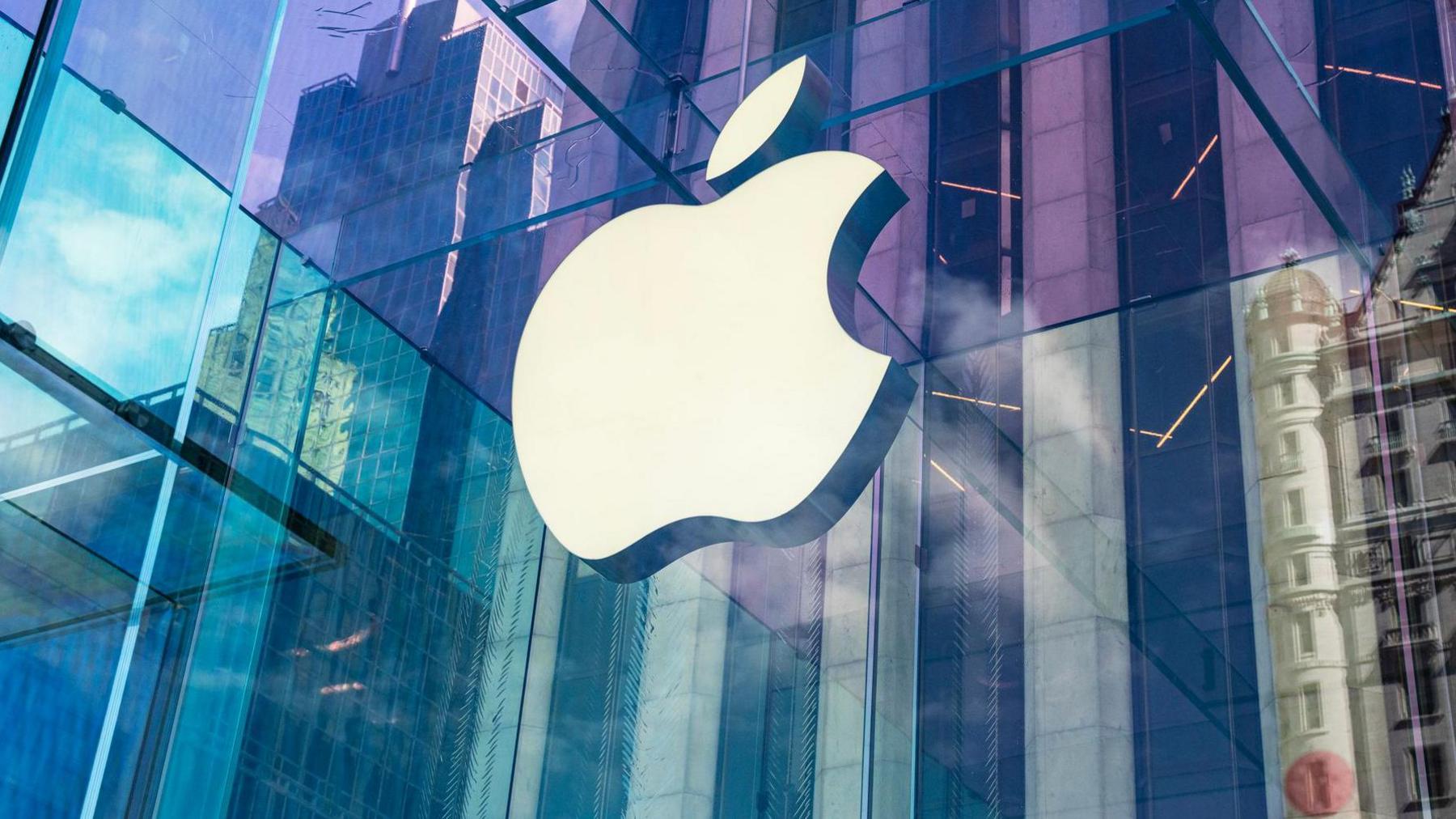 The Apple logo on a window, with a city scene including skyscrapers reflected on the window