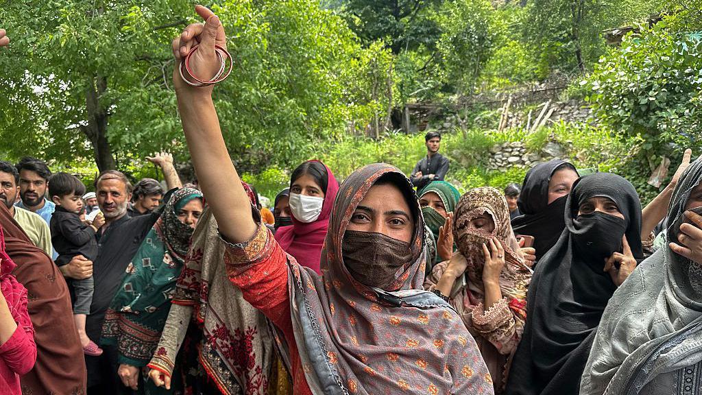 A crowd of protesters, mainly women, gathers, with some raising their hands. their faces are covered with headscarves.