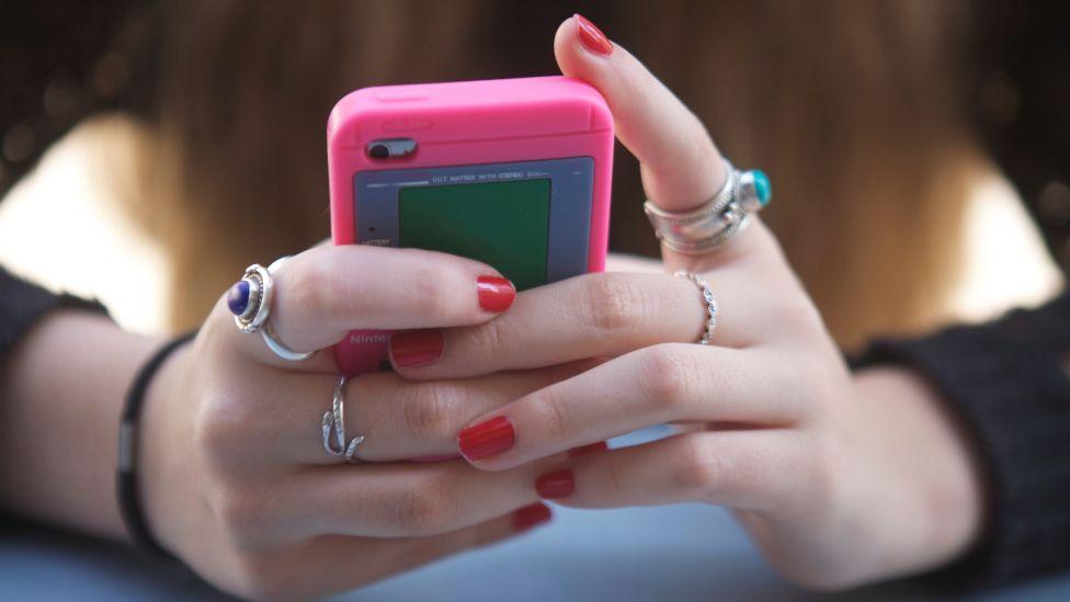 A smartphone is seen in the hands of a teenager girl