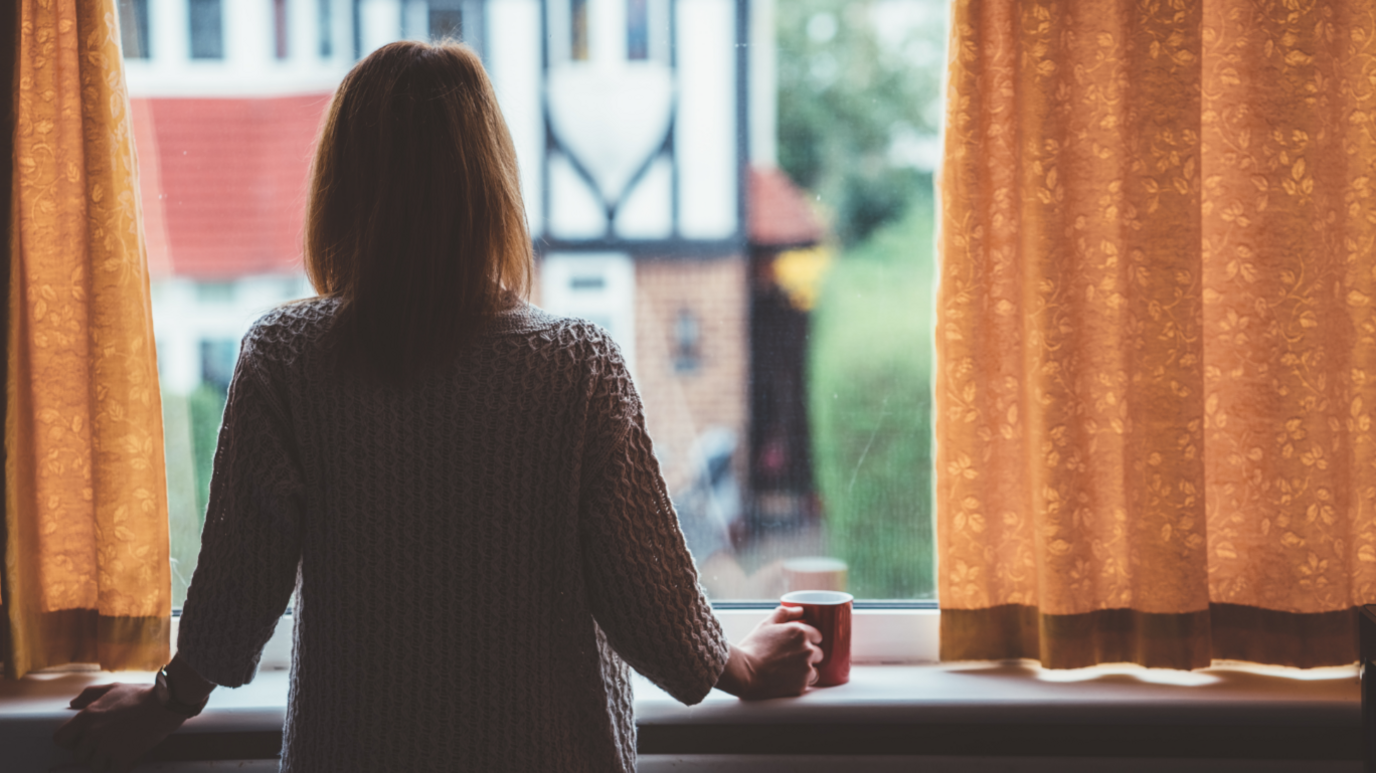 Rear view of woman at home staring through the window