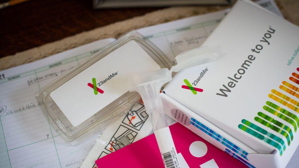 A home DNA testing kit is spread out on a table, with a saliva collection tube and packaging prominently displayed. The branding 23andMe is clearly visible, as are the words 'Welcome to You' along with lots of coloured lines in the shape of a swab.