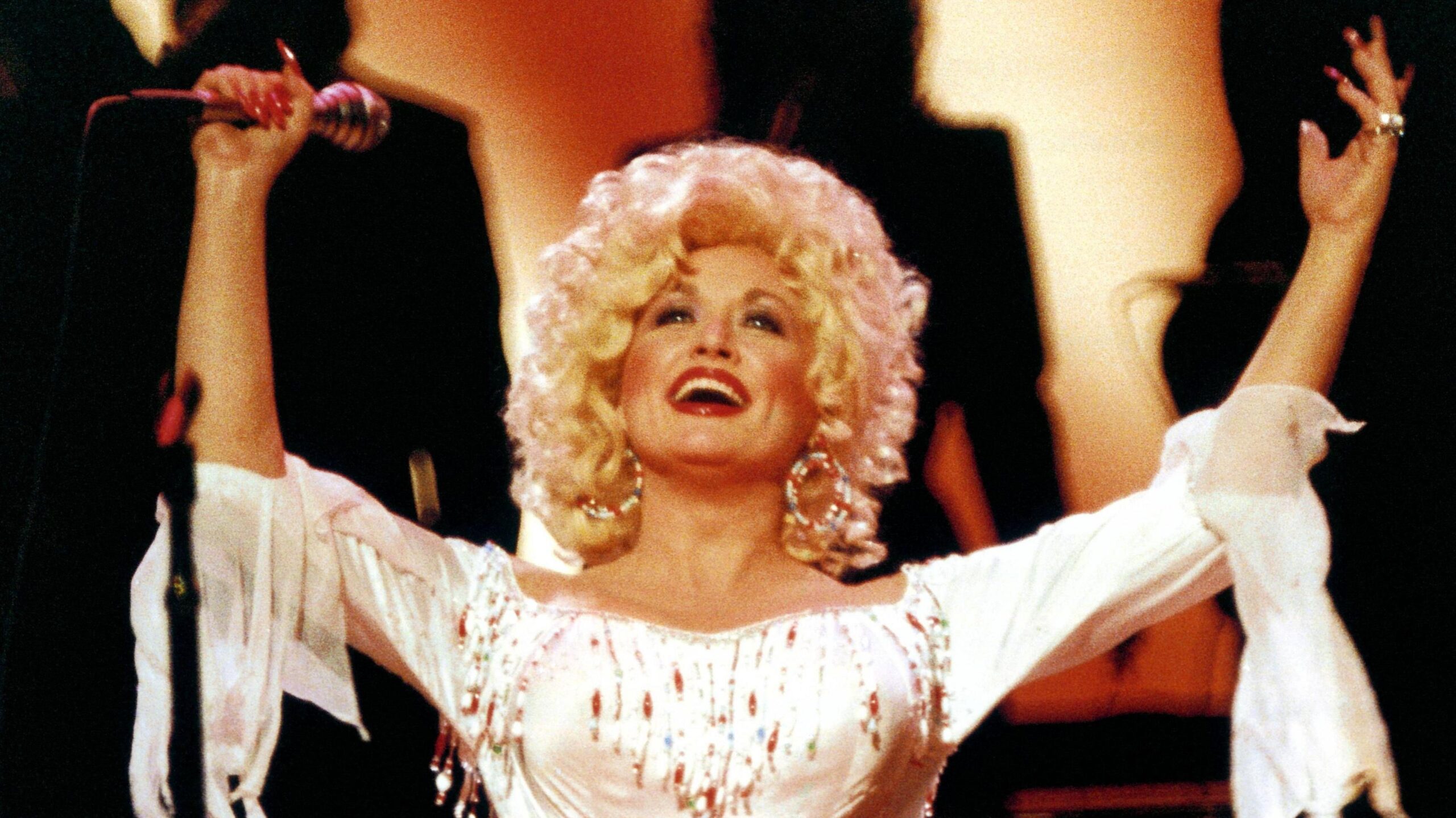 Dolly Parton with both arms raised on stage in 1983