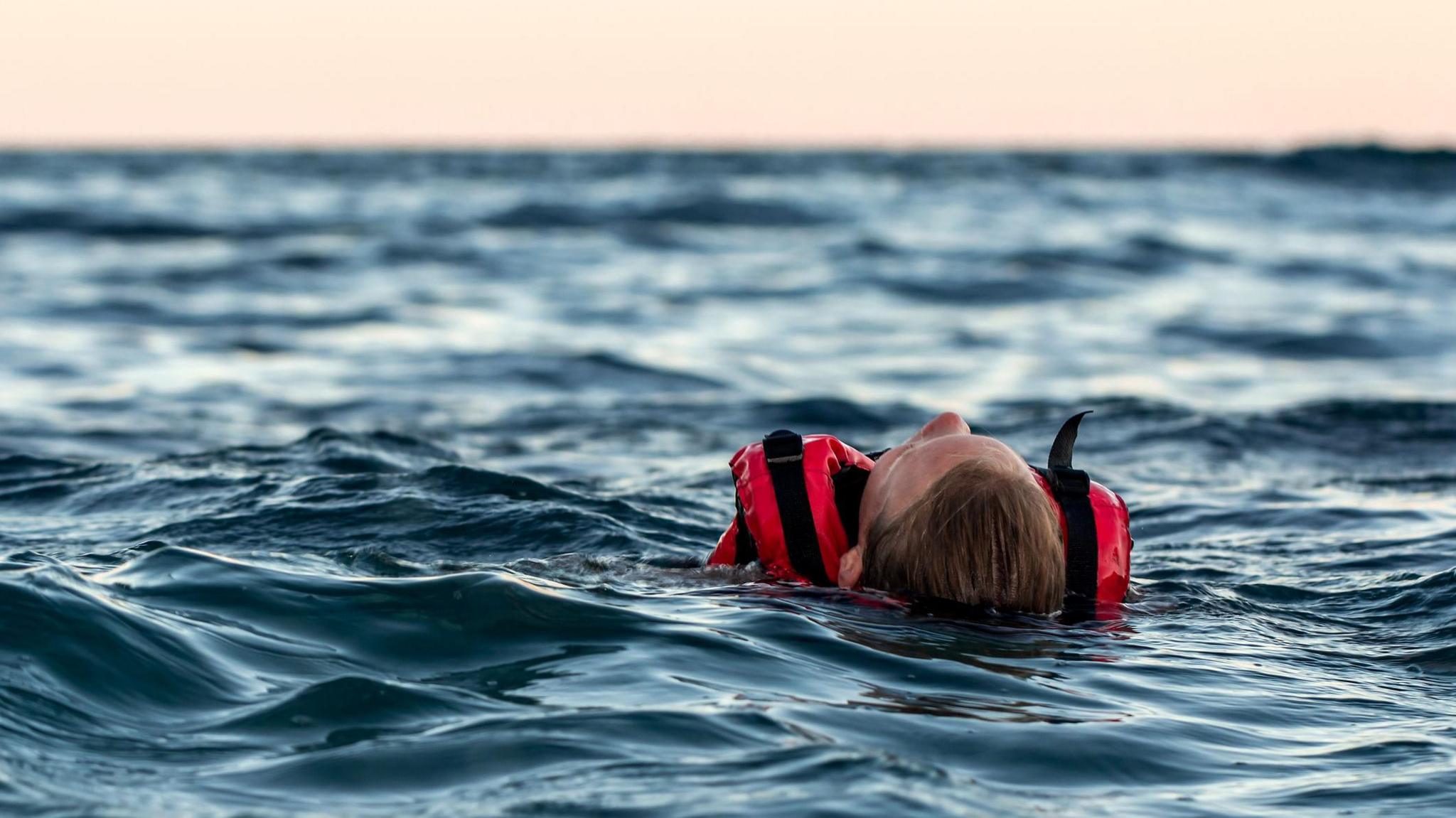 A person lying in open water wearing a red life vest