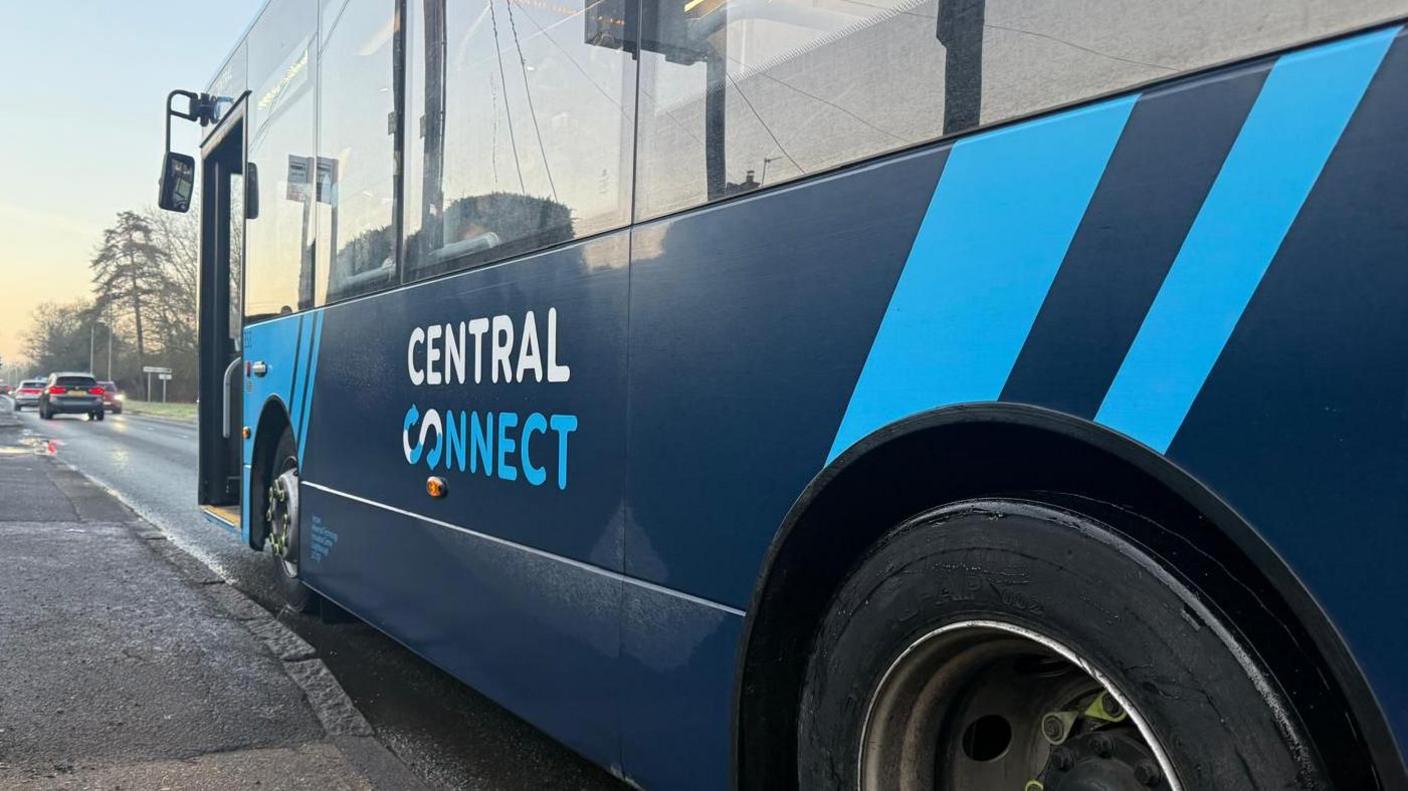 The side of a blue bus parked at a bus stop. Its door is open. The logo of the bus operator Central Connect is printed on the bus in blue and white lettering.