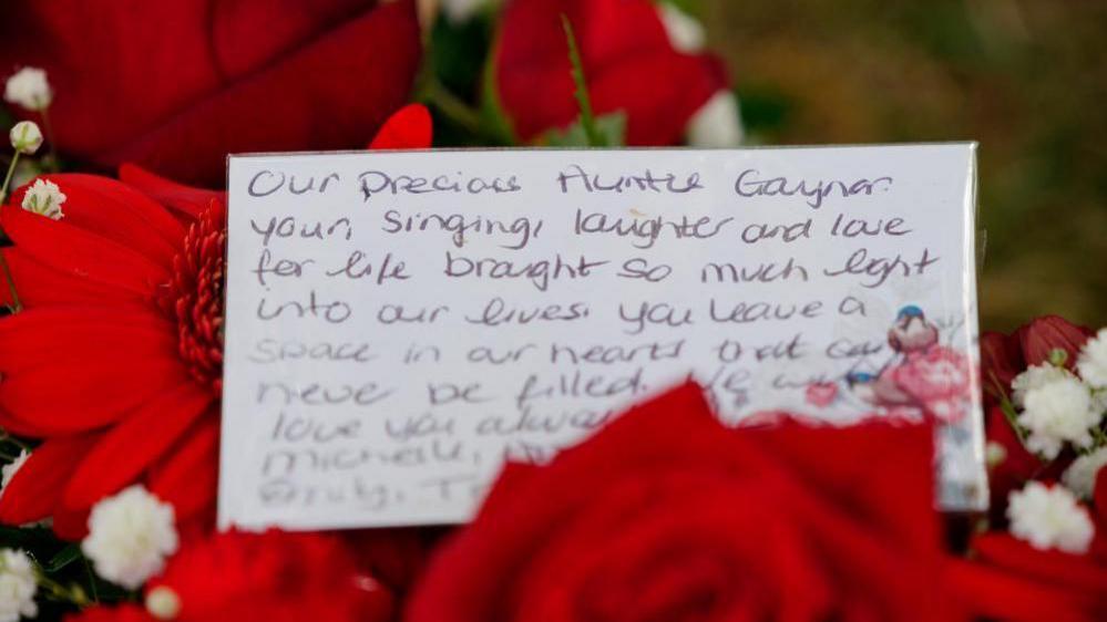 A message on a card attached to a floral tribute includes the words ‘Our precious Auntie Gaynor. Your singing, laughter and love for life brought so much light into our lives. You leave a space in our hearts that can never be filled.’