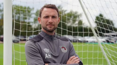 Image shows Alex Hughes, 37, wearing his grey Grimsby Town training top and standing in front of a set of goals.