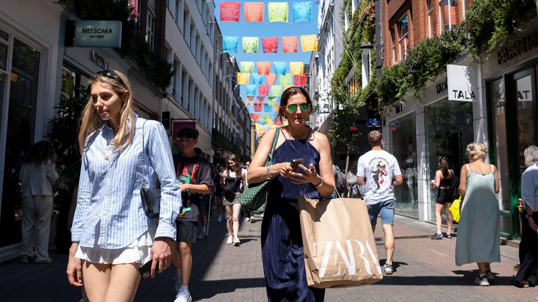 two shoppers on a busy shopping street in London walking towards the camera wearing summery clothing