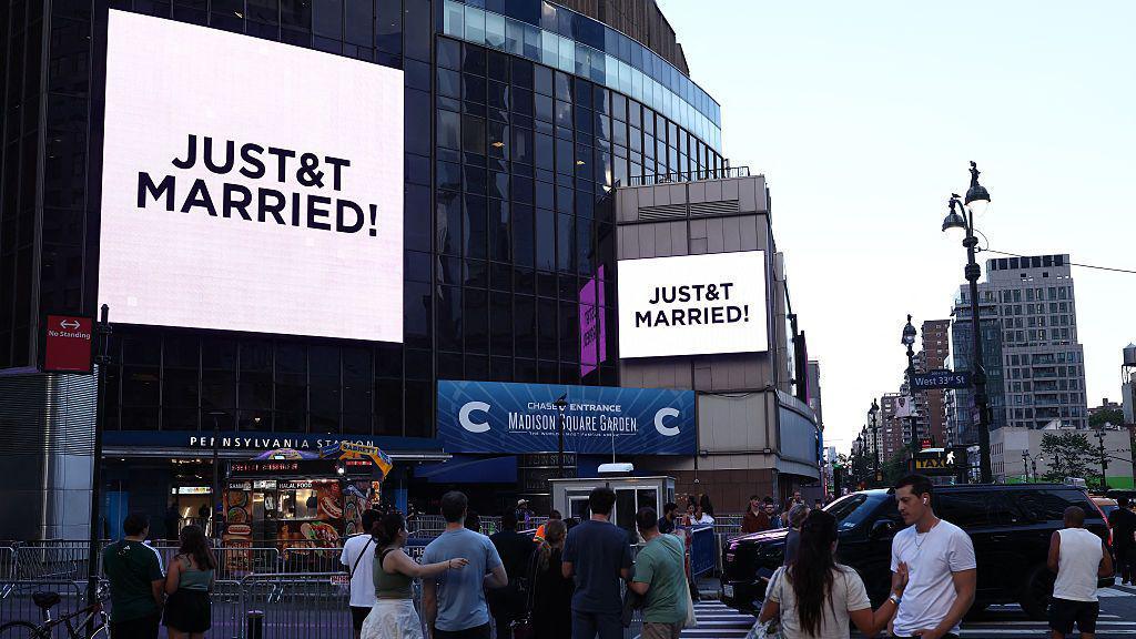 People watch giant screens showing the message "JUST&T MARRIED!" (T&T for Taylor and Travis) outside Madison Square Garden, the reported venue for the wedding celebrations of pop singer Taylor Swift and pro-athlete Travis Kelce, in New York City on July 3, 2026.