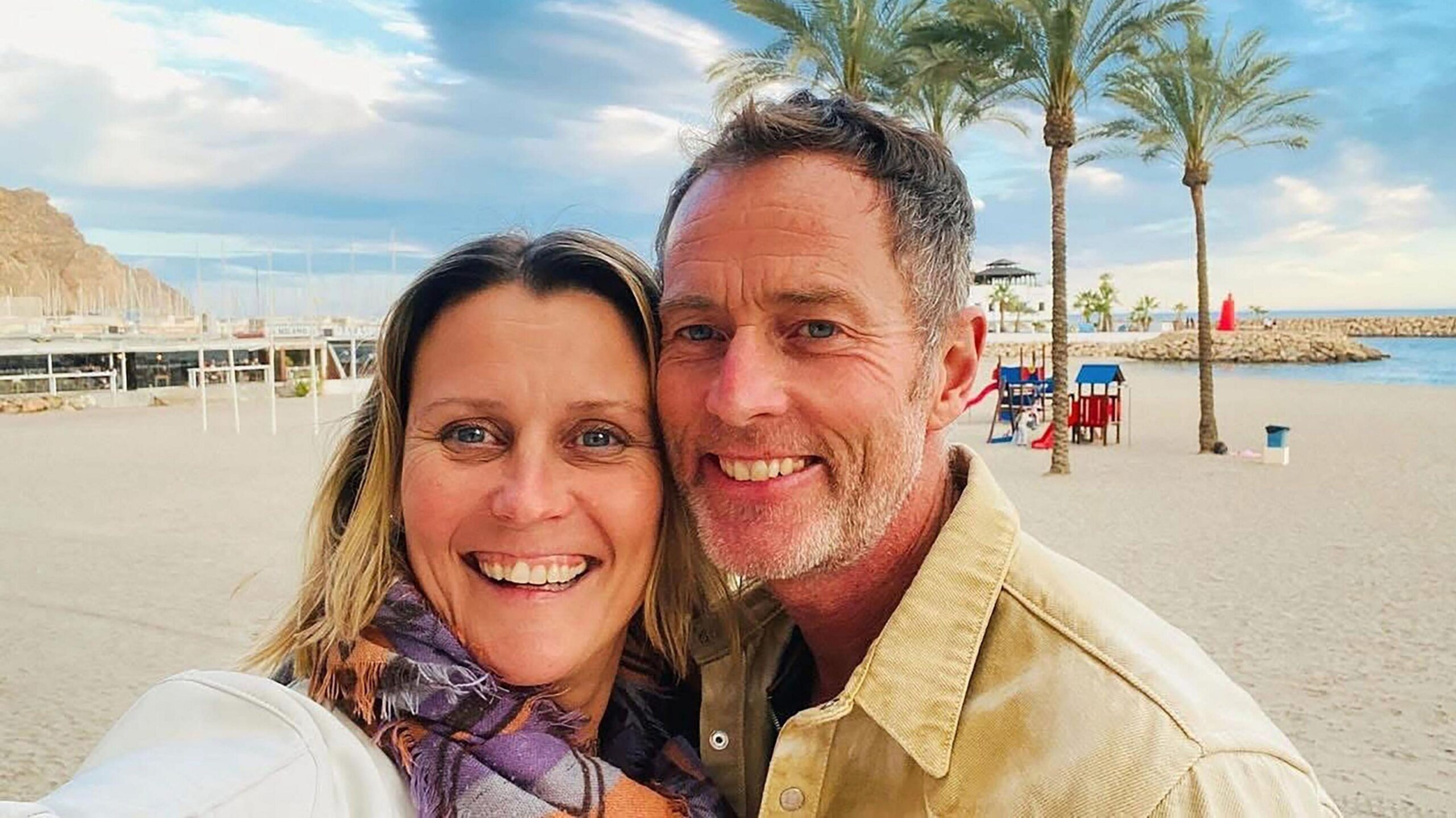 A middle-aged couple on a beach. They are smiling.