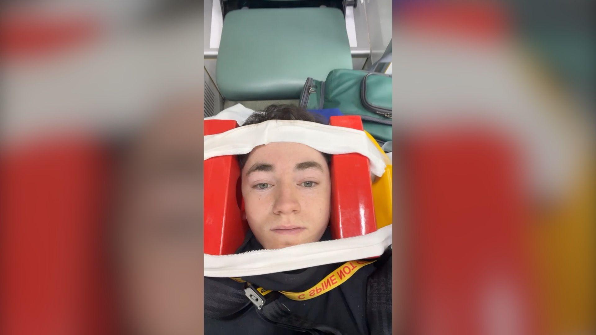 A selfie of Taylor in the ambulance after a crash caused by e-bike riders. He has red padded blocks either side of his head and pale material across the top and bottom of his face and wrapping around the back of the blocks. He is looking at the camera.