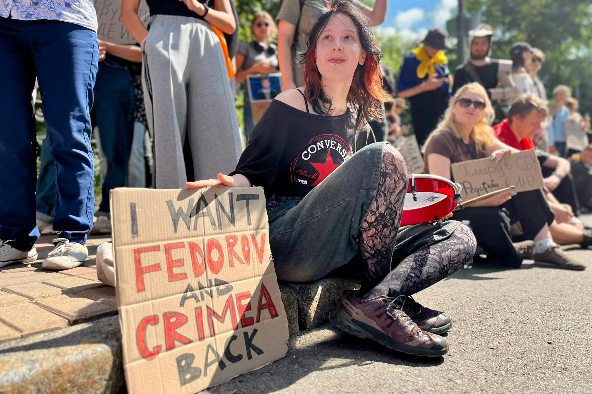 A woman sits beside a placard saying "I want Fedorov and Crimea back"