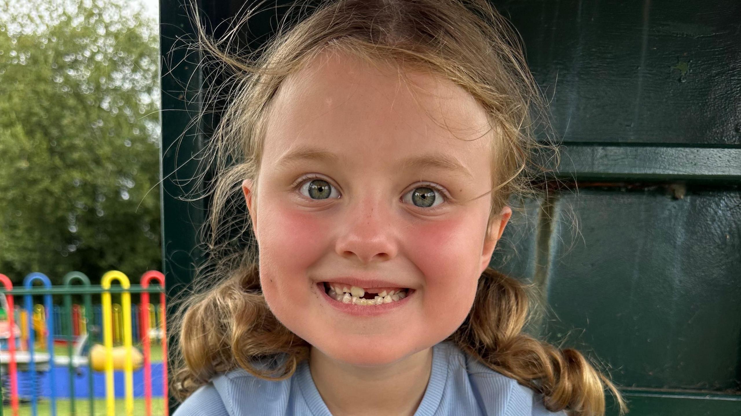 A young girl with curly hair in two bobbles. She is smiling and looking at the camera.