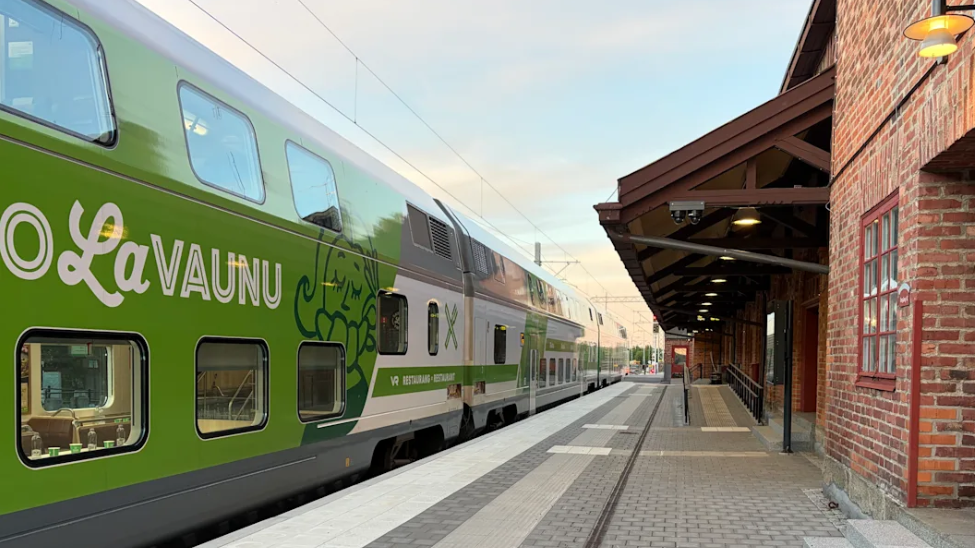 A green and white double-decker Finnish VR train pulls into a railway station.