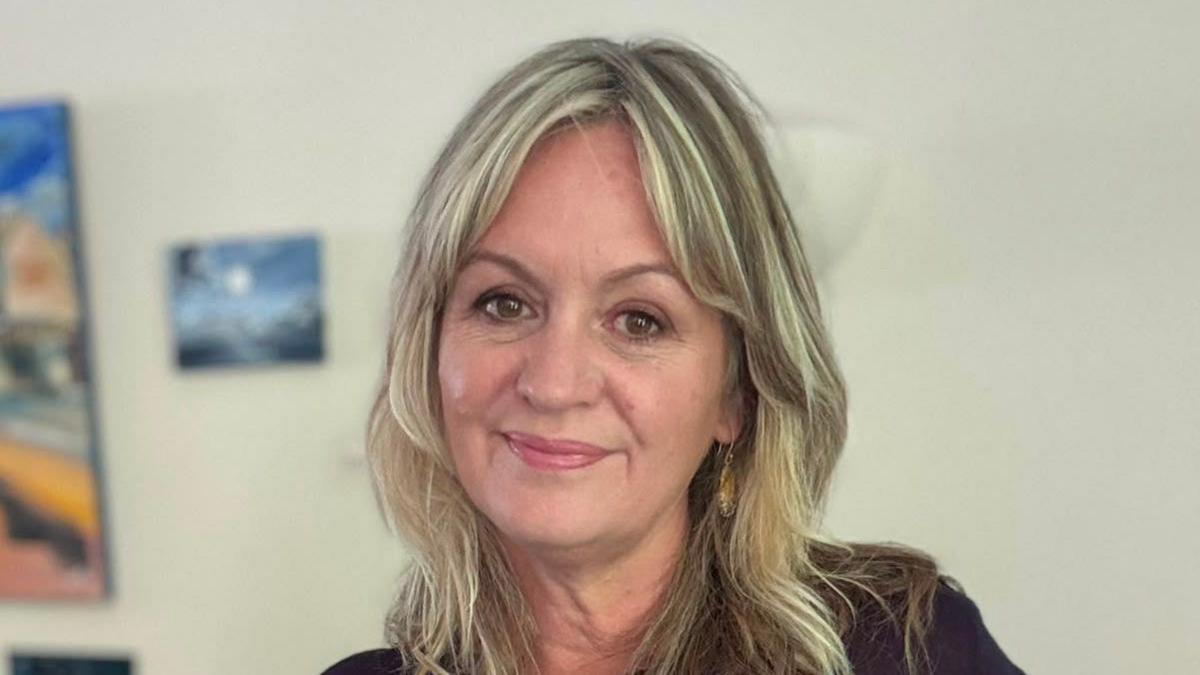 A woman with long blonde hair looks at the camera