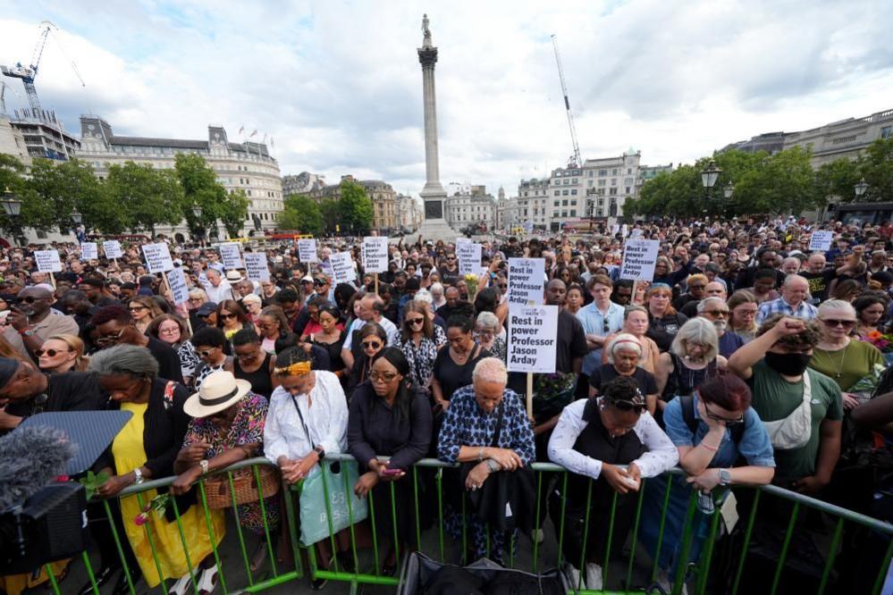 A crowd of people gather in Trafalgar Square as part of a vigil for Jason Arday. Some of them are holding placards.