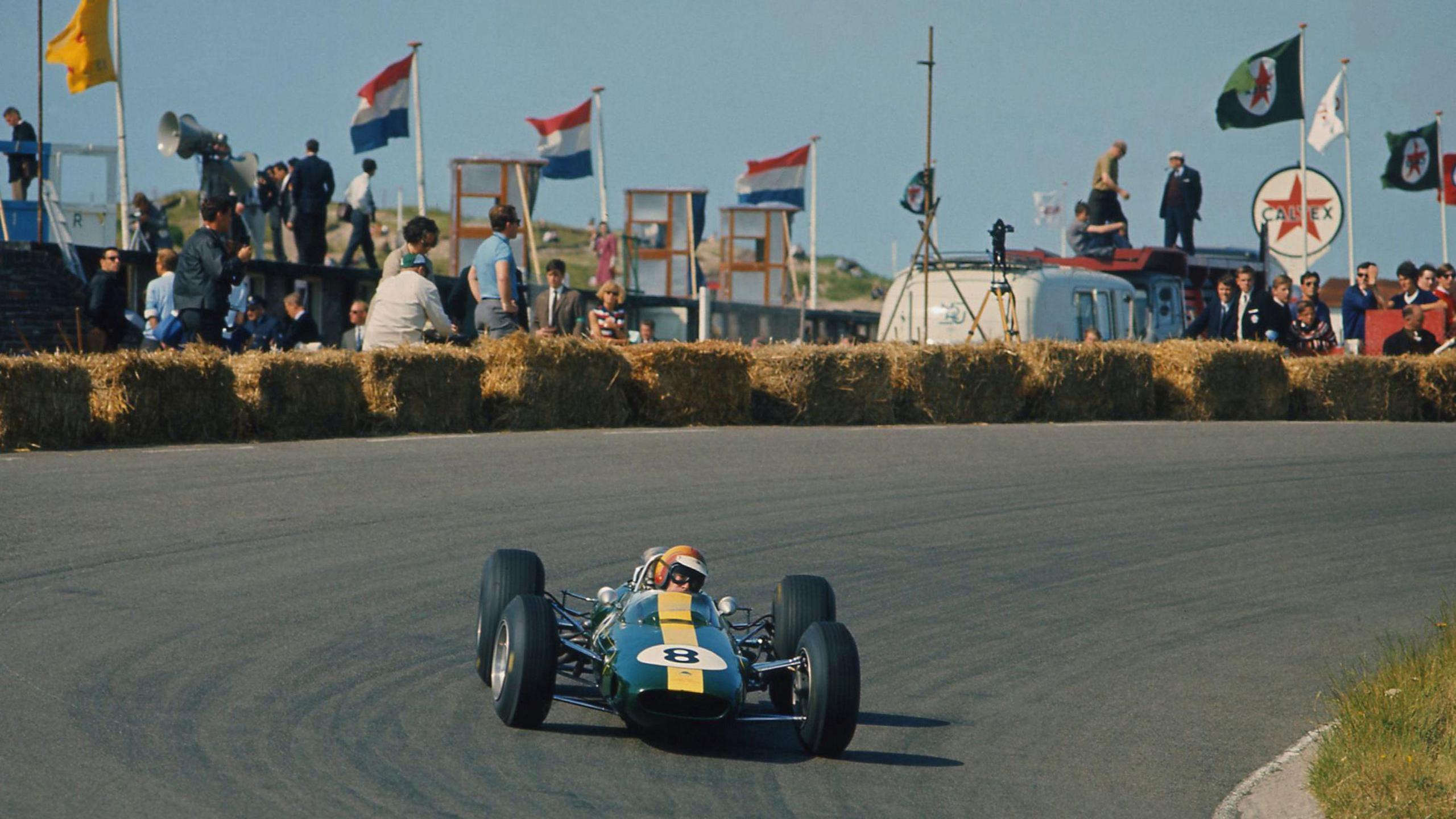 Jim Clark driving his Lotus during the 1965 Dutch Grand Prix. The Netherlands flag is flying in the background