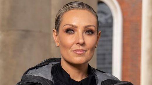 Amy Dowden pictured in a promotional photo for the Channel 4 show, Celebrity Hunted. Amy is wearing a black top, jacket and coat. She is looking at the camera and not smiling.